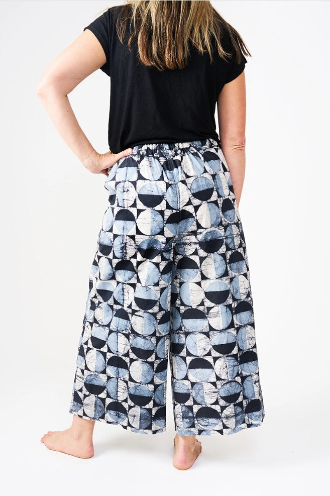 Person wearing a black top and patterned blue and white pants on a white background