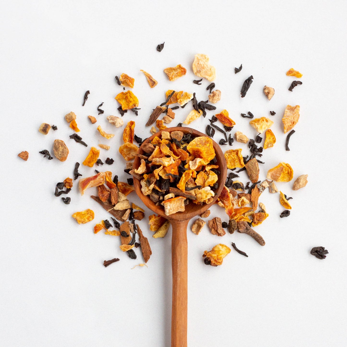 Wooden spoon filled with a mix of dried orange peels and black tea leaves on a white background