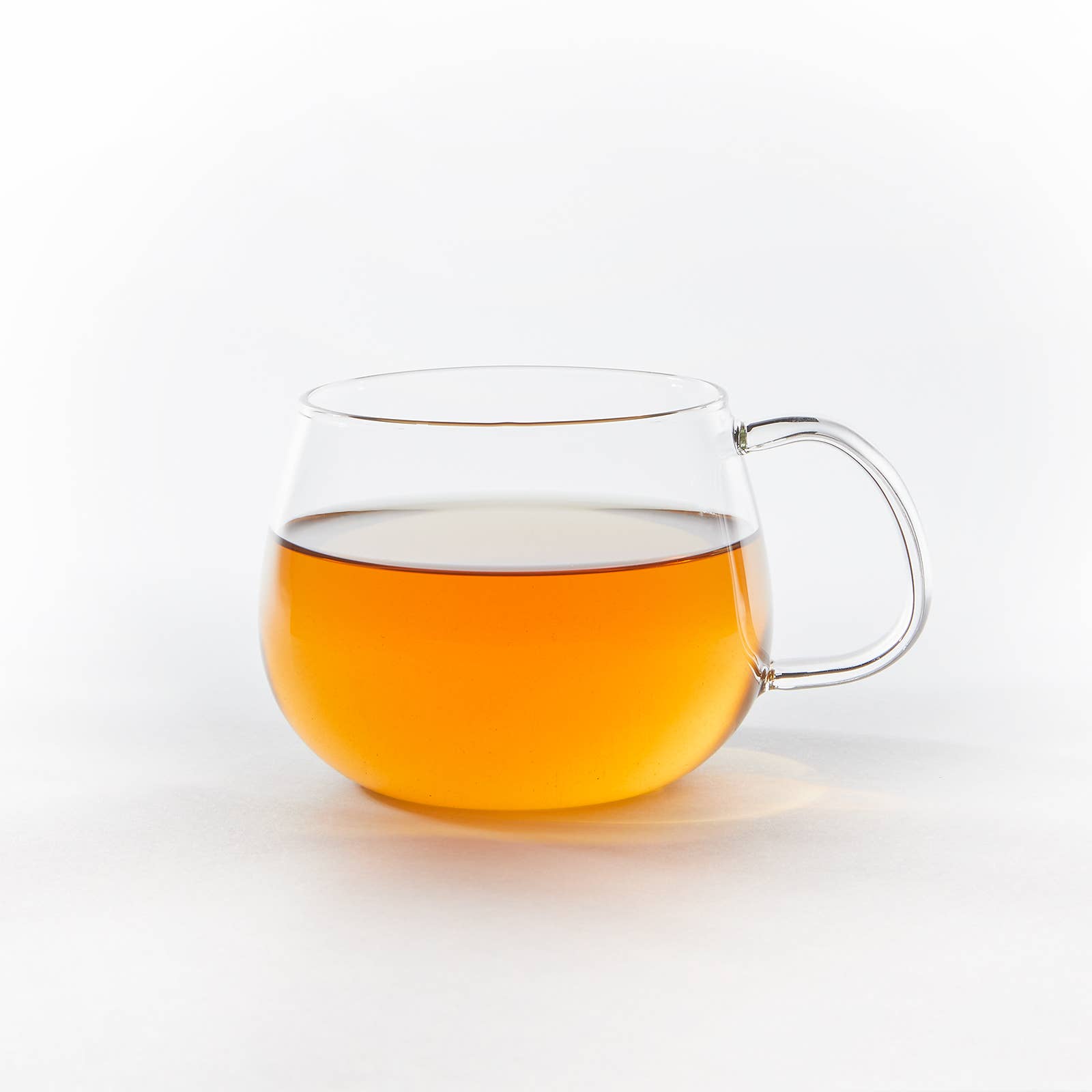 Clear glass mug with a handle filled with orange liquid on a white background