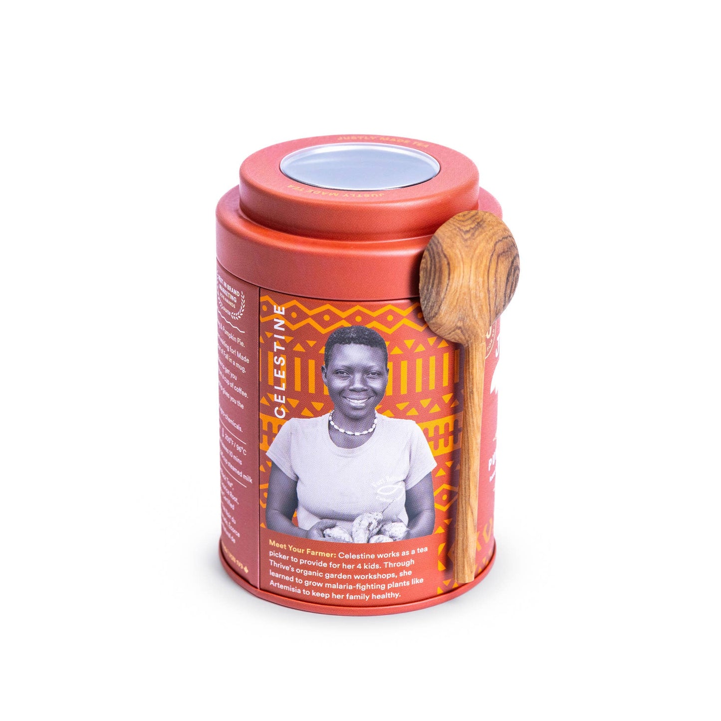 A cylindrical tea tin with a terracotta red lid and base, featuring an orange and black geometric patterned label with a portrait of a woman. A wooden spoon rests on the side of the tin, and the product is photographed on a clean white background.
