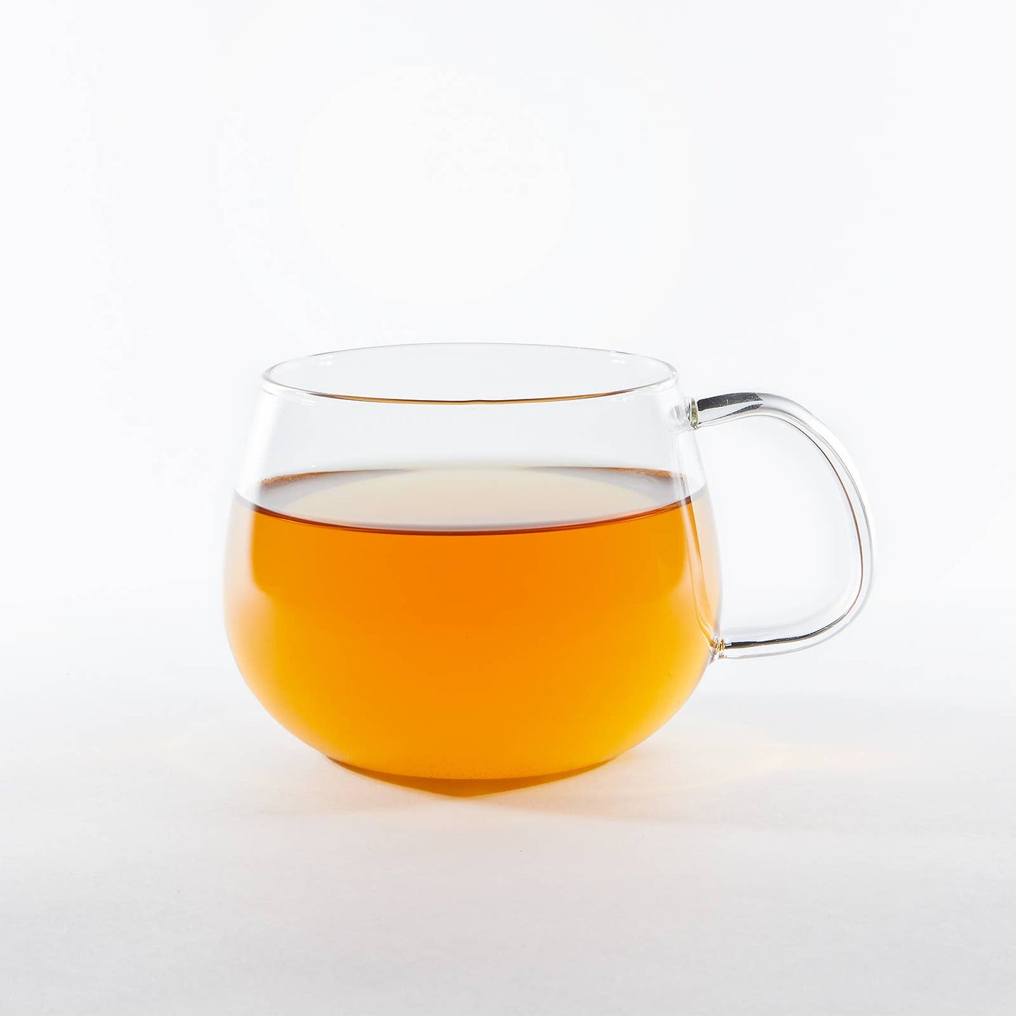 Clear glass mug filled with a warm beverage on a white background
