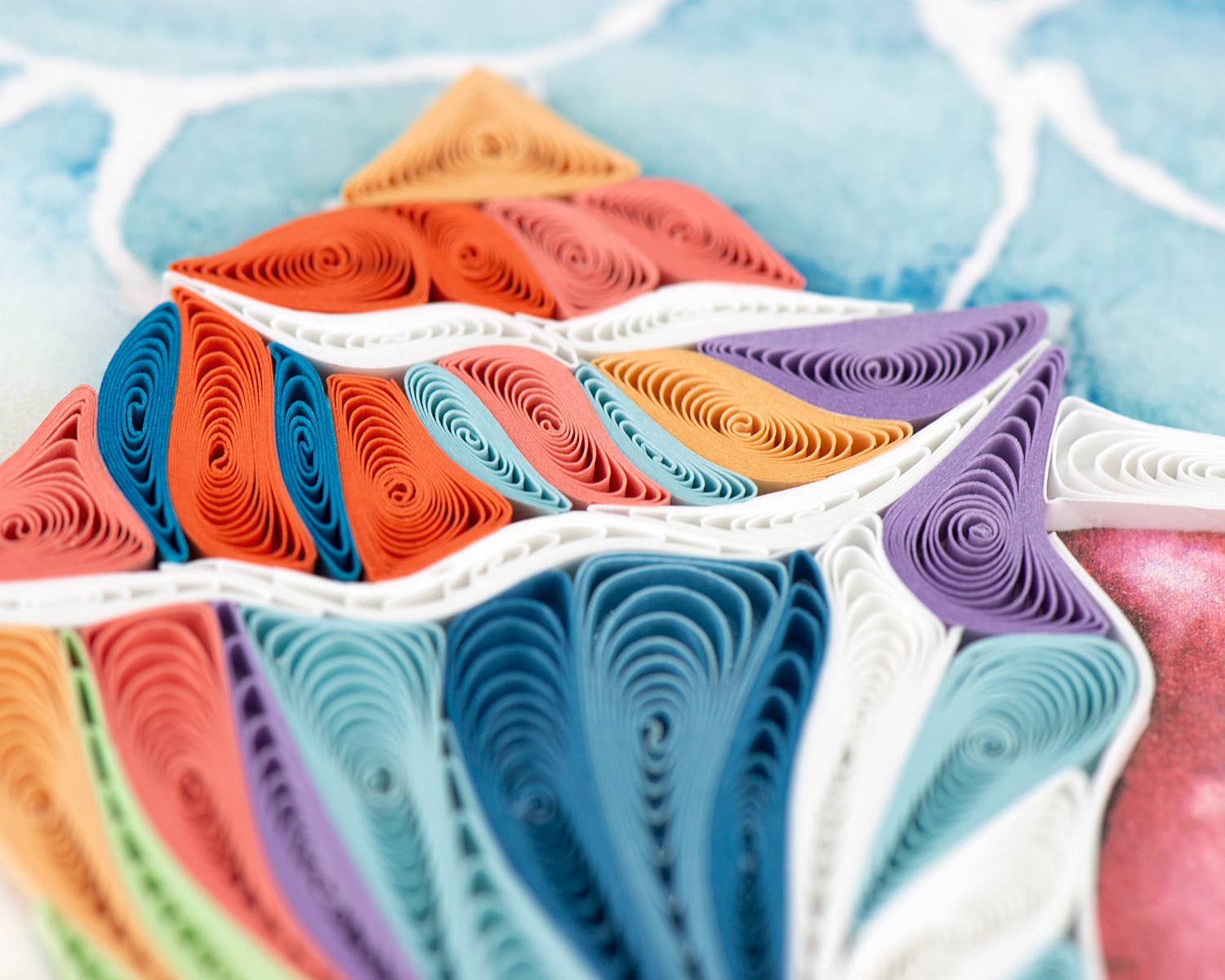 A rainbow of colored paper is arranged to create the shape and pattern of a conch shell.