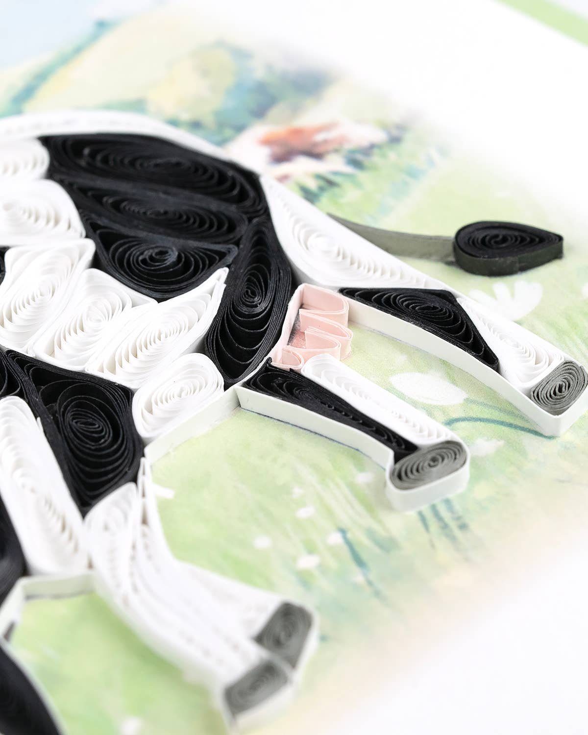 Black and white quilled shapes are arranged to create a cow's legs, tail, and udder.