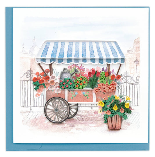 A push cart filled with quilled flowers is covered with a striped blue and white awning.