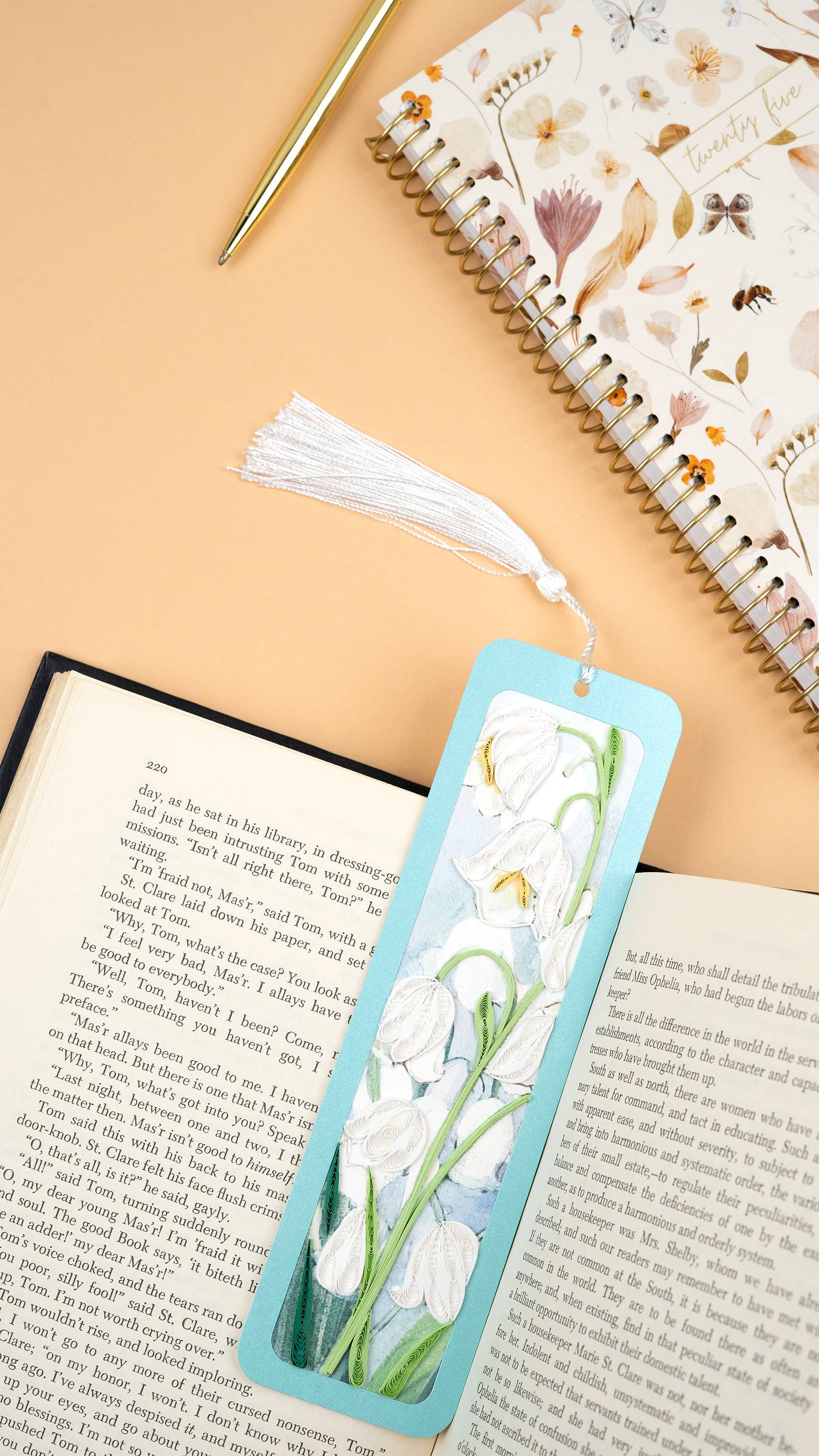 A blue bookmark with a white flower design and a white tassel are displayed in an open book.
