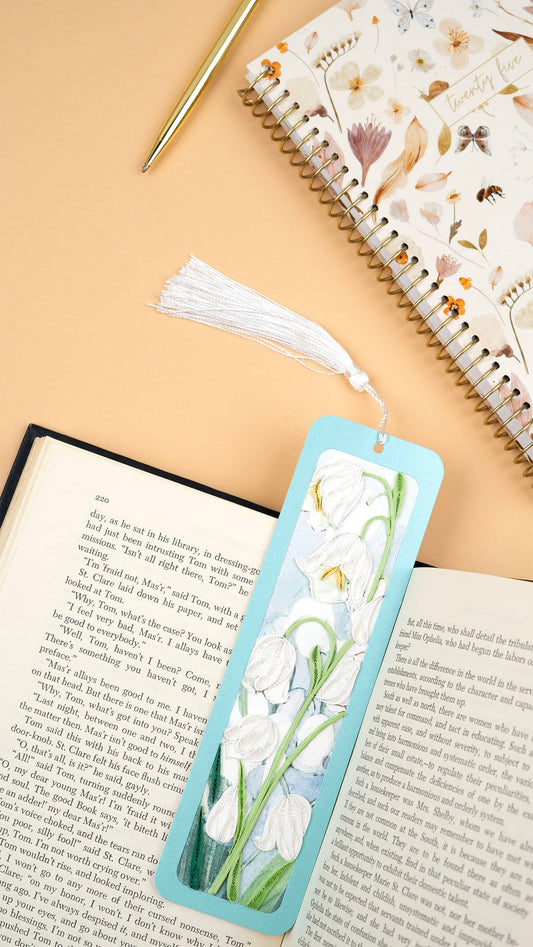 A blue bookmark with a white flower design and a white tassel are displayed in an open book.