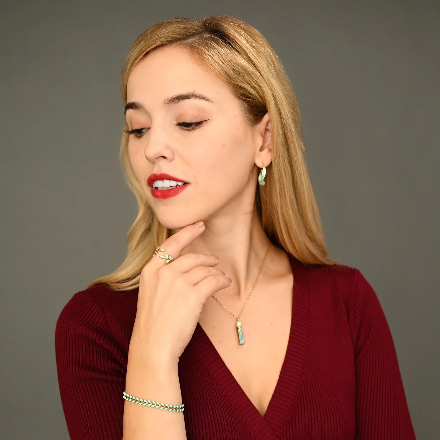 Woman wearing a red top and gold and mint colored jewelry against a gray background