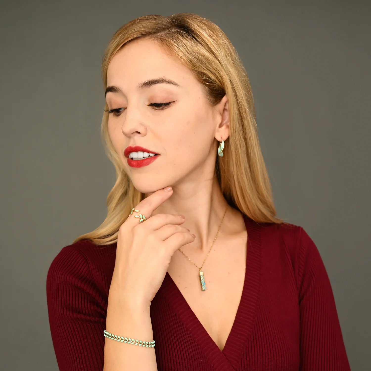 Woman wearing a red top and gold and mint colored jewelry against a gray background