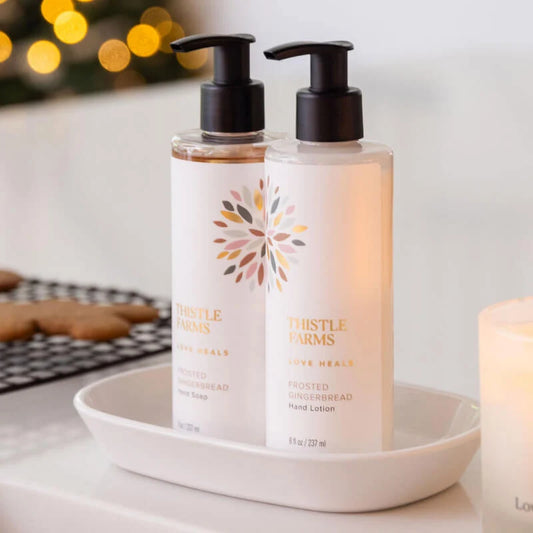 2 Clear bottles with black pump on a white dish with gingerbread men cooling on a white countertop.