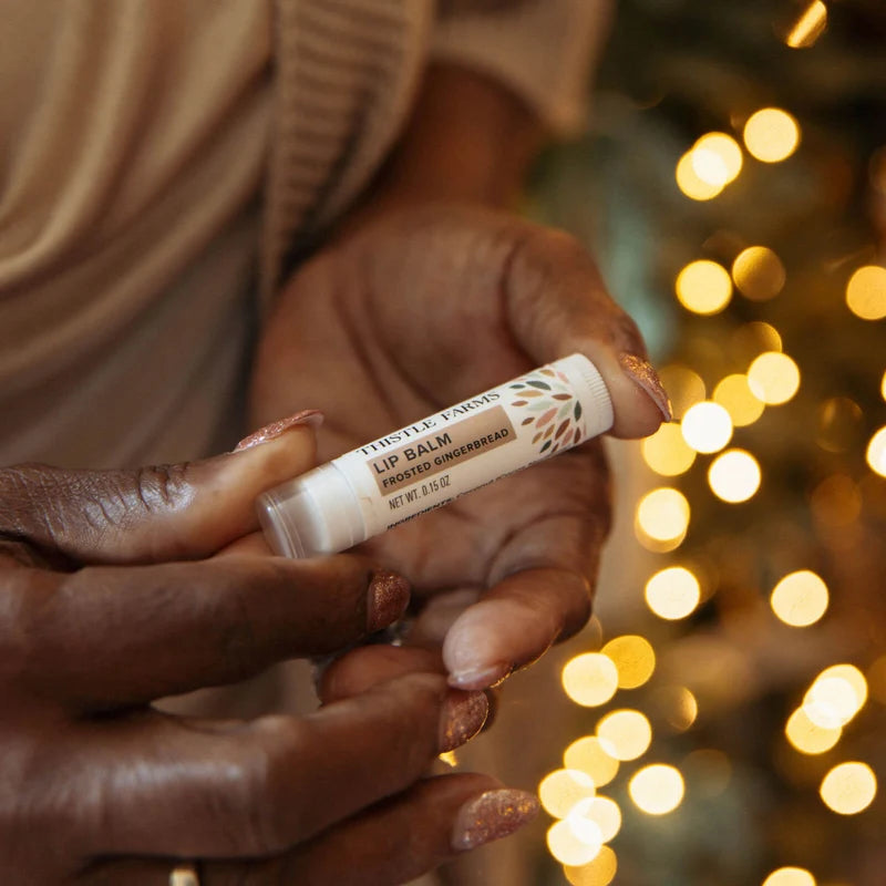 White Lip balm tube with tan decoration being held with a Christmas tree in the background