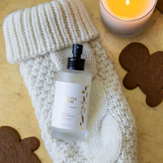 Frosted glass bottle with black lid on a white knitted stocking with gingerbread man cookies and a candle