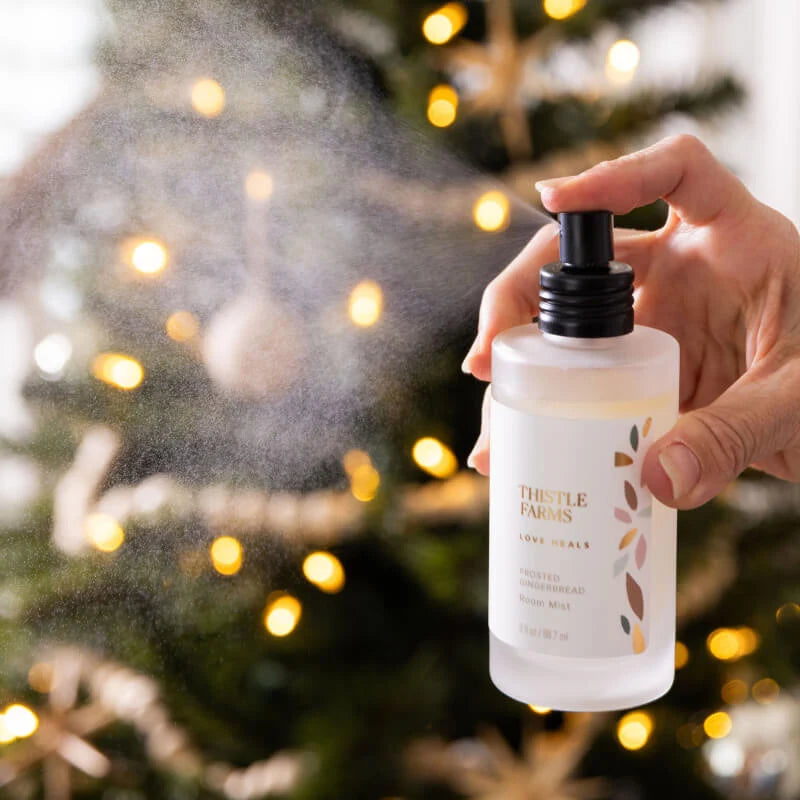 Frosted glass bottle with black lid being sprayed in a room with a Christmas tree in the background