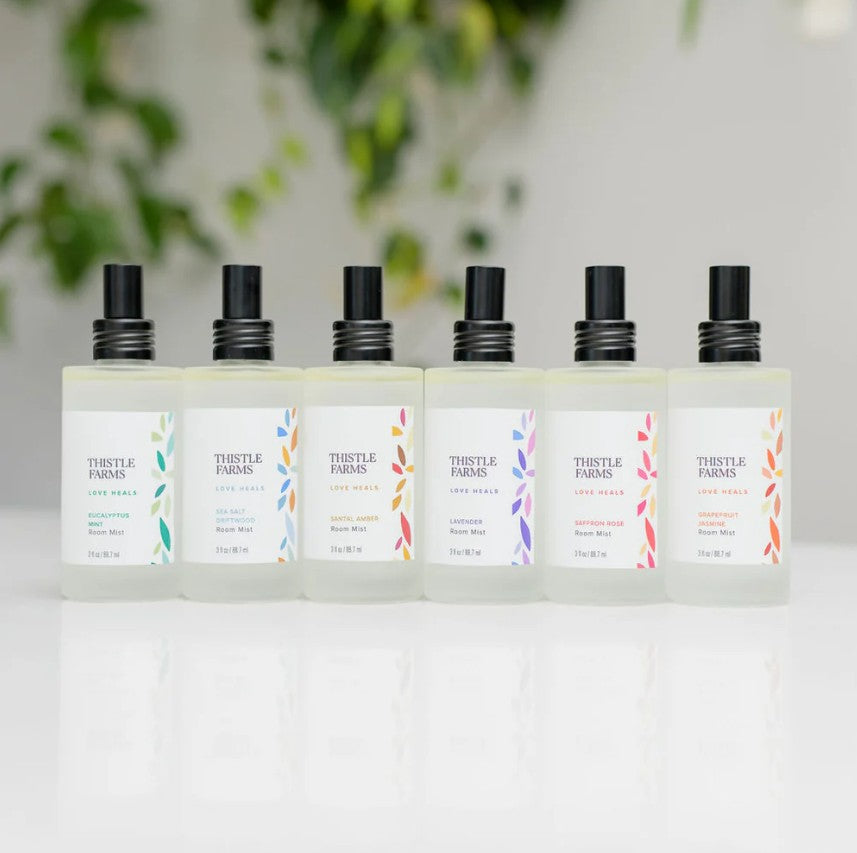 Set of Thistle Farms products on a white surface with a blurred green plant background