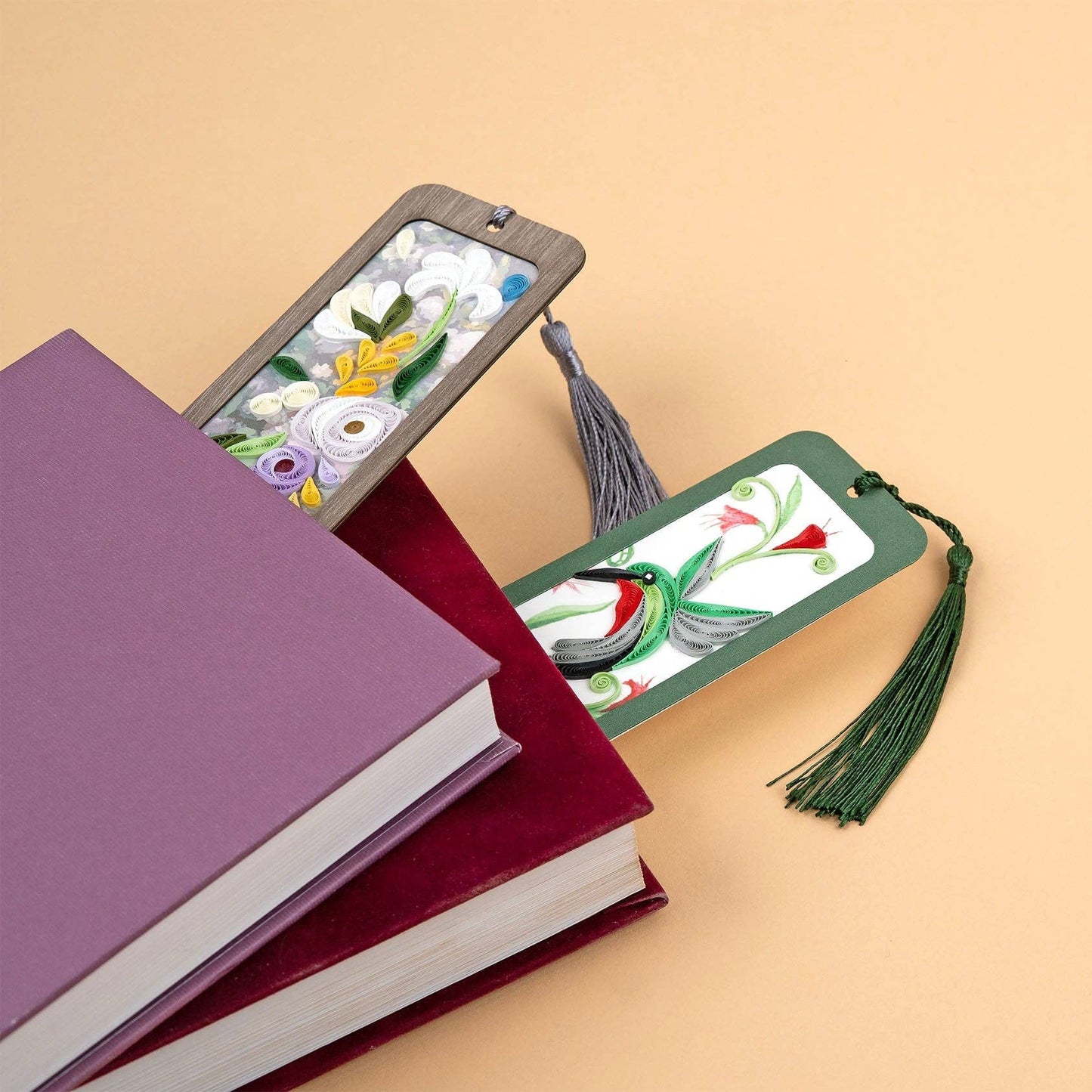 One green hummingbird bookmark and one floral bookmark stick out of the end of two separate books.