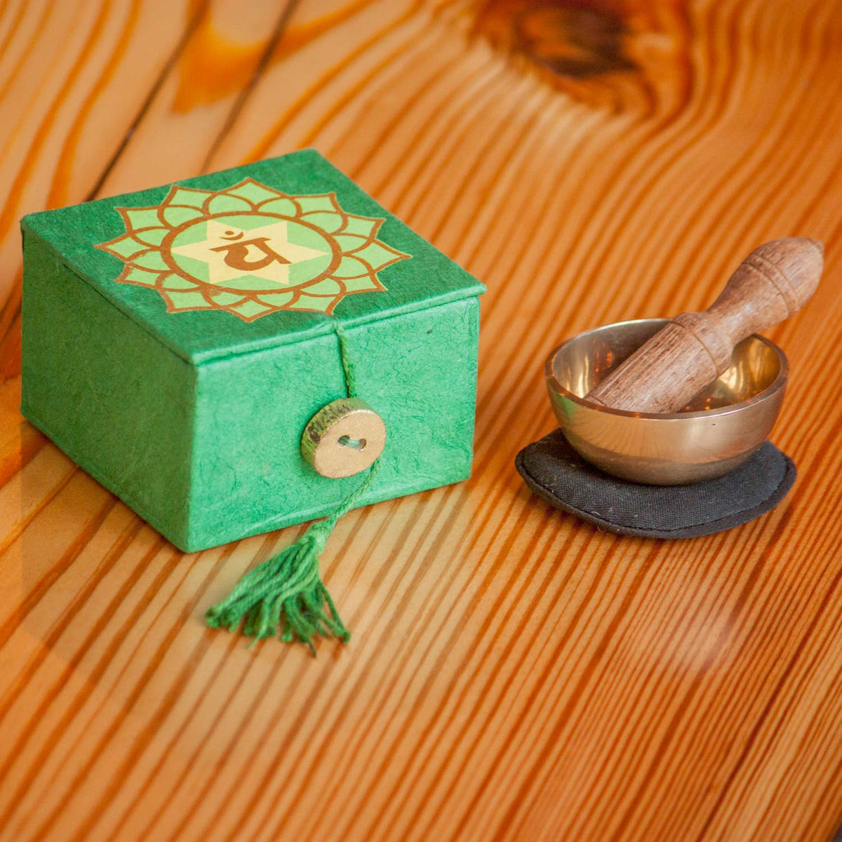 Green box with decorative emblem on a wooden surface next to a small metal bowl and wooden striker.