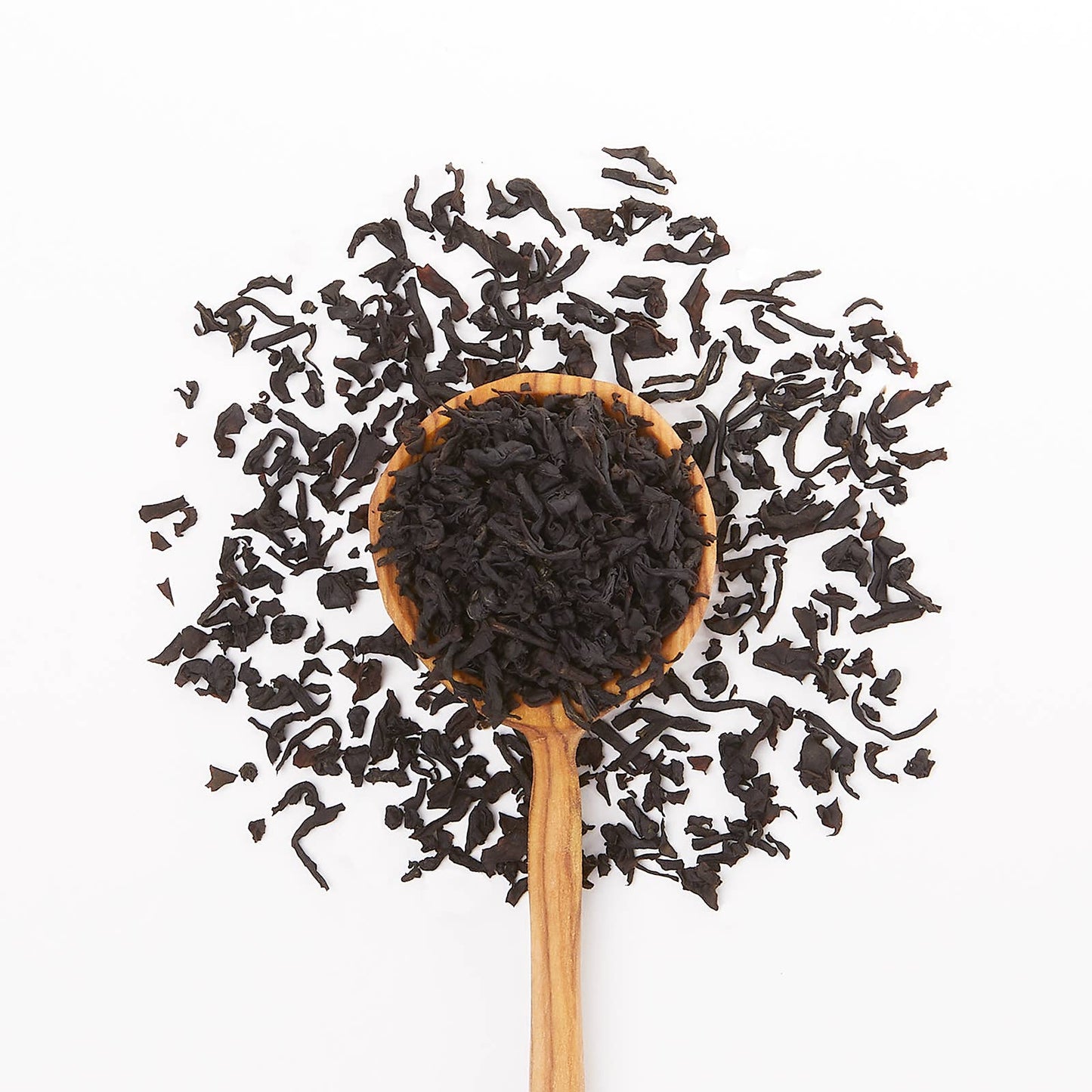 Wooden spoon filled with black tea leaves on a white background