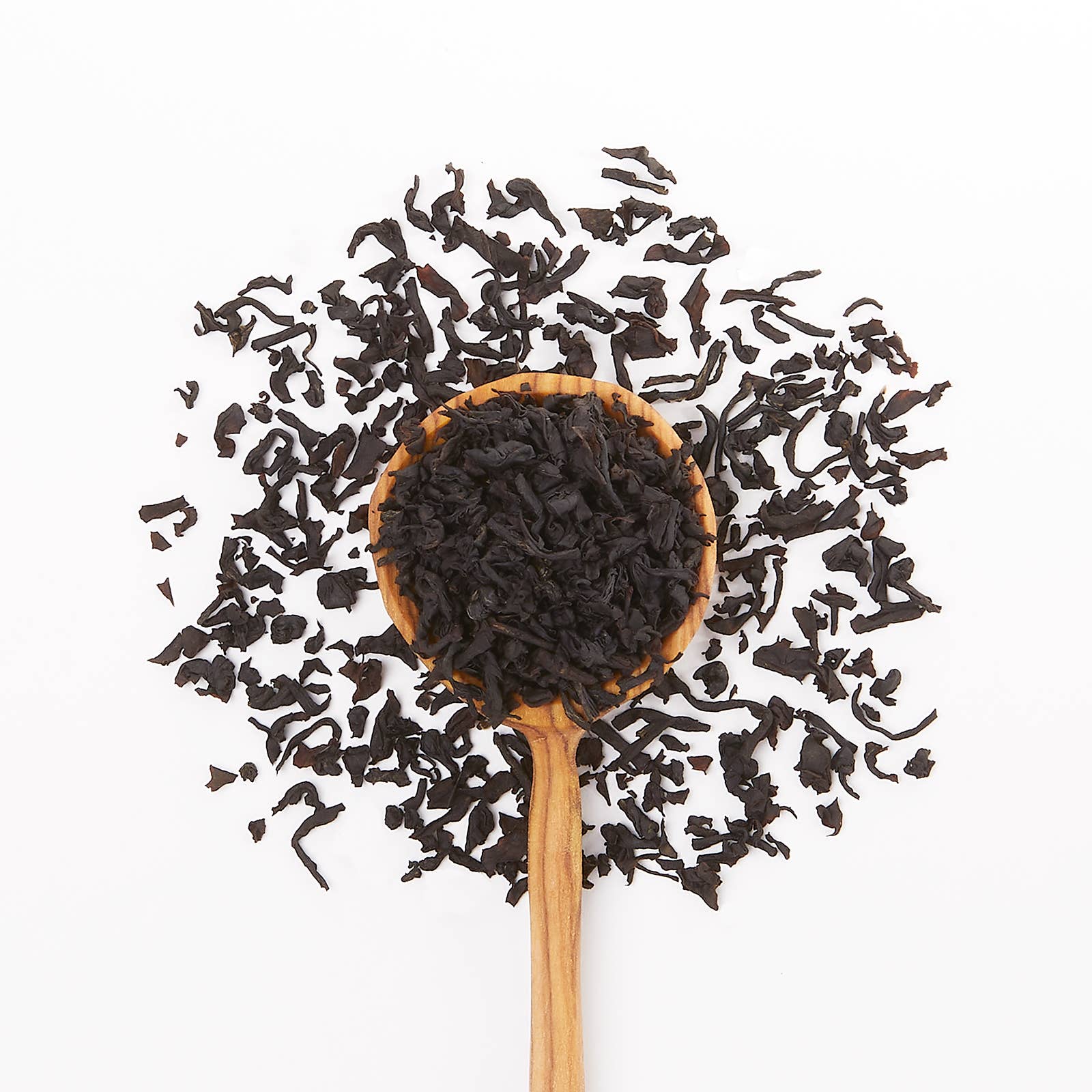 Wooden spoon filled with black tea leaves on a white background