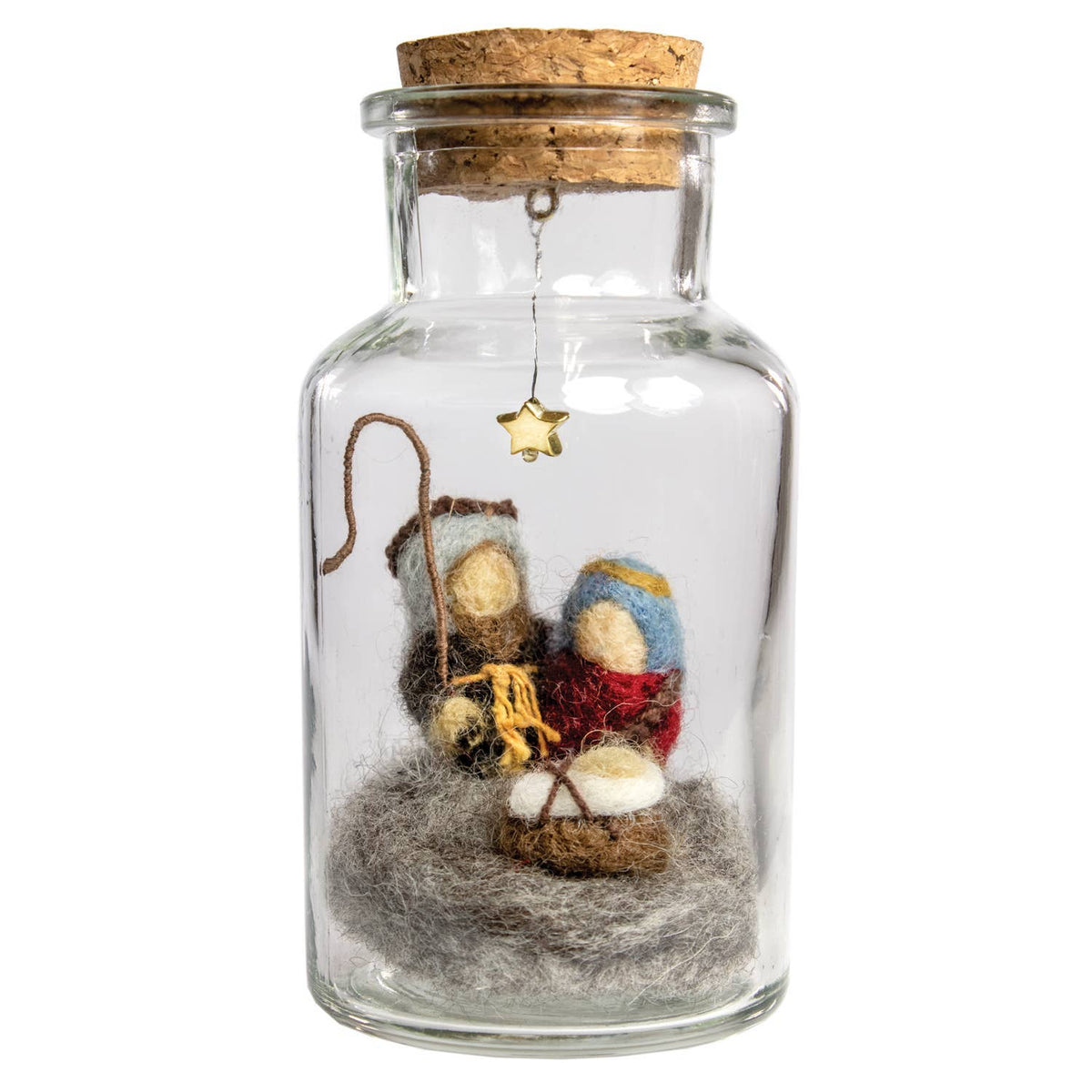 A small glass bottle with a cork stopper containing a miniature nativity scene. Inside, two felted wool figures in blue and red robes sit beside a manger with a star hanging from the neck, all set on a bed of gray felted wool.