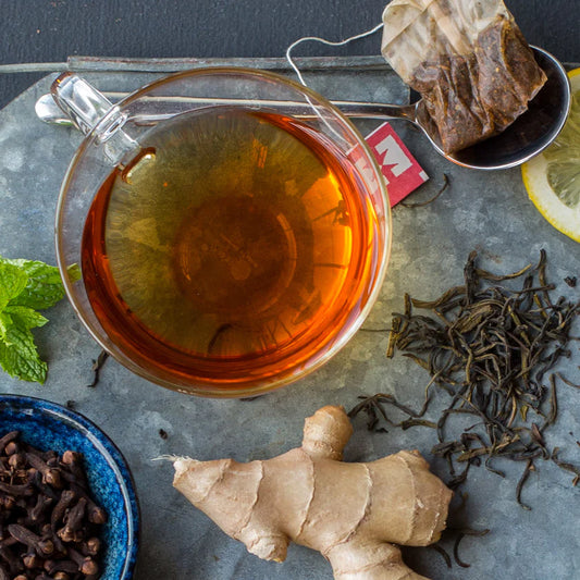 Tea cup with brewed tea, tea leaves, ginger root, and spices on a gray surface.