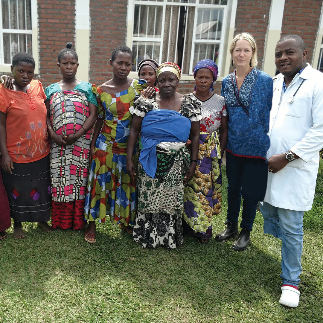 Group of women and a doctor standing together outdoors, with a building in the background.