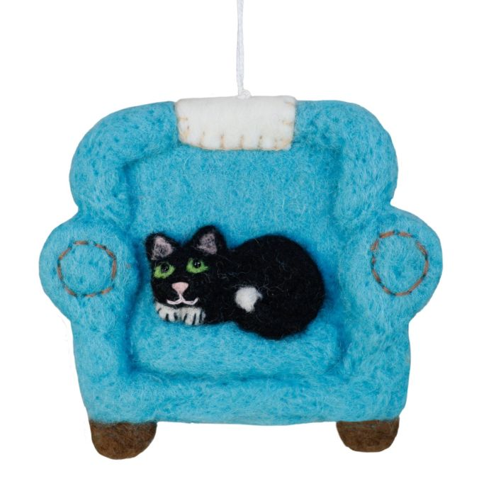 A felt Christmas ornament shaped like a small blue armchair with a black cat figurine sitting inside, hanging by a white string against a plain white background.