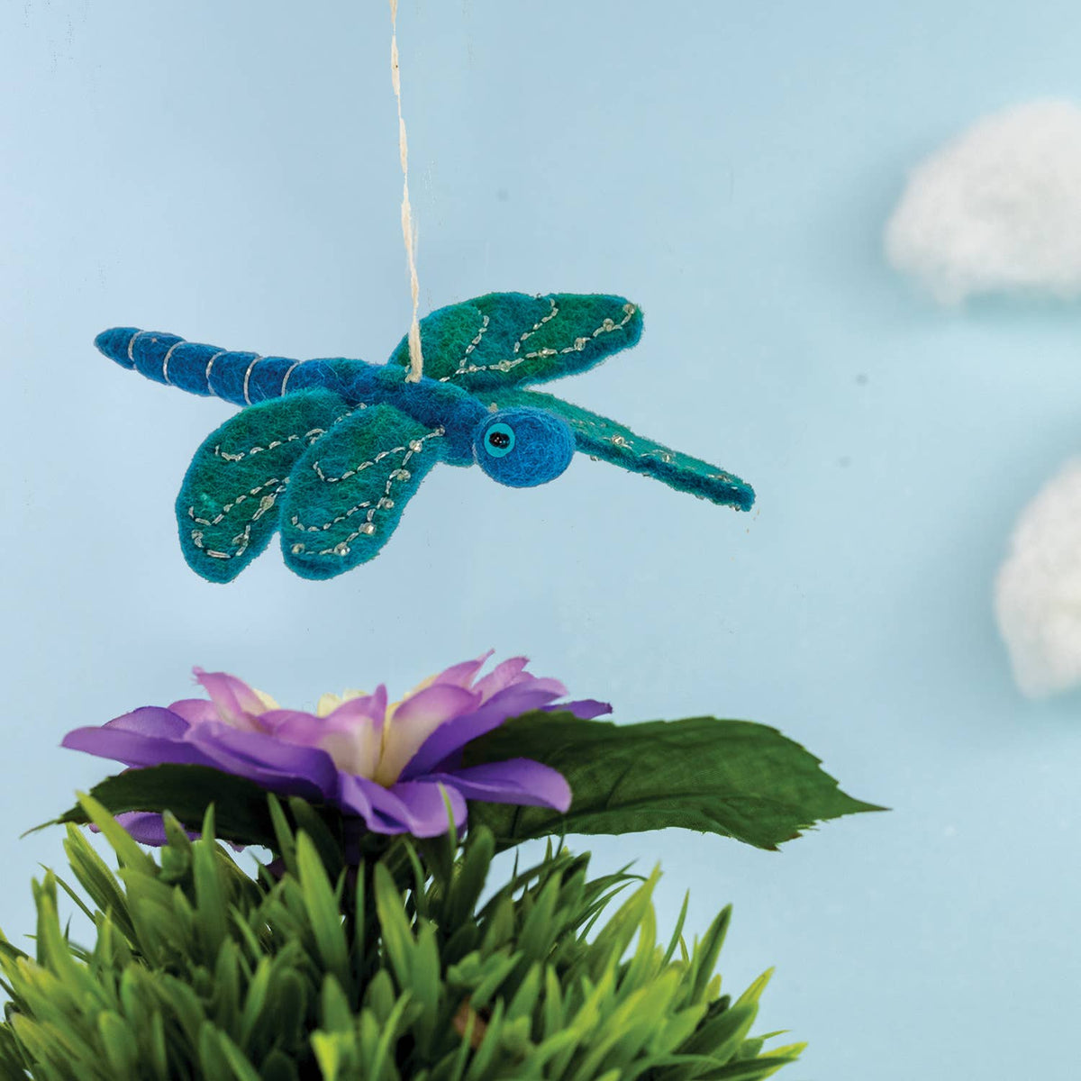 Decorative dragonfly hanging above a purple flower with a blue background
