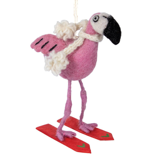 A pink felt flamingo ornament wearing a white fluffy scarf and red felt skis, hanging by a white string against a plain white background.