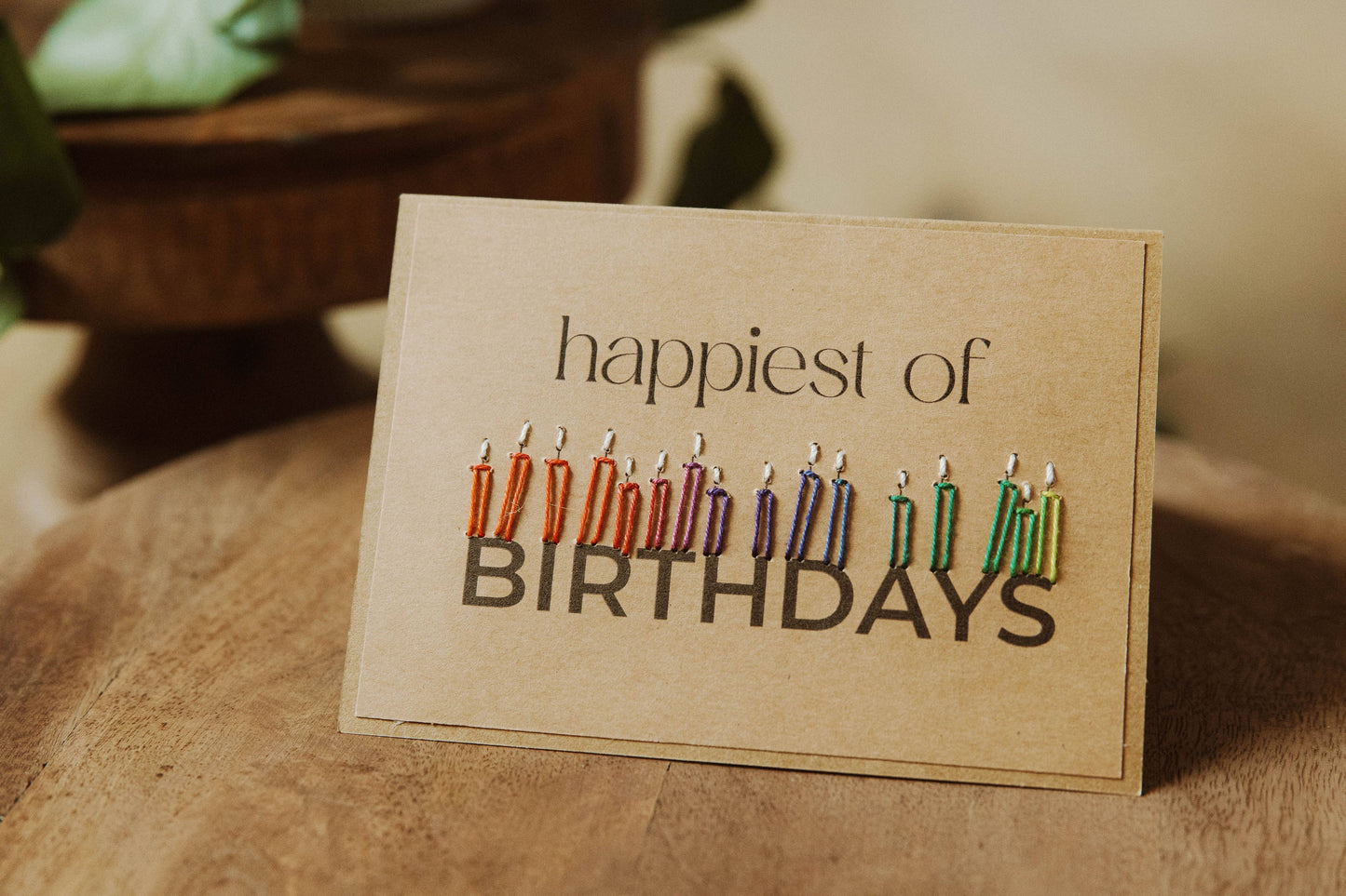 Greeting card with colorful candles and 'happiest of birthdays' text styled on a wooden surface.
