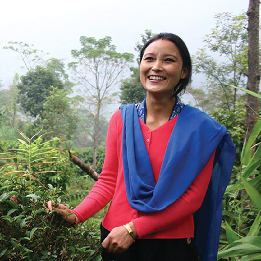 Smiling woman standing in a lush tea plantation.