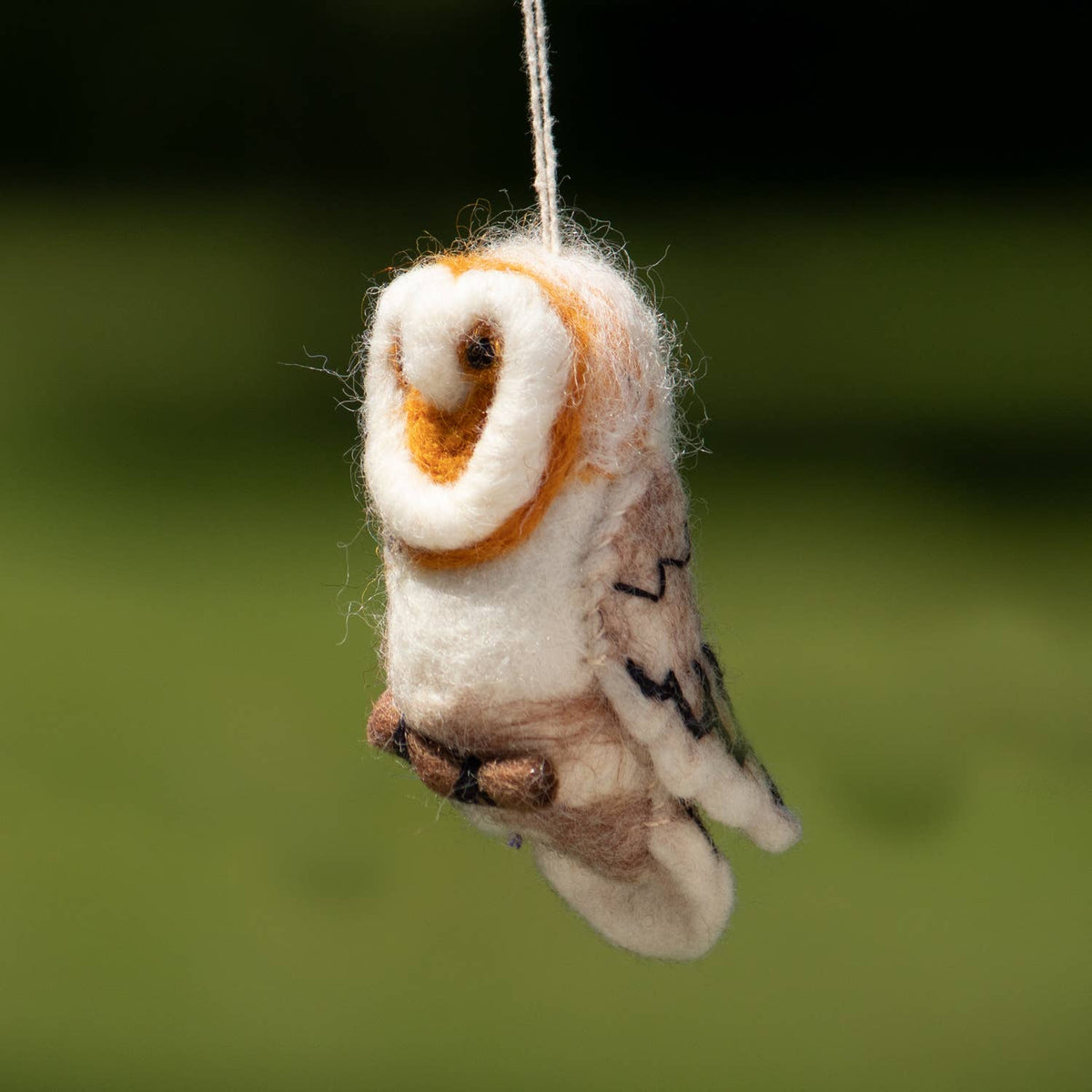 Felted owl ornament hanging against a blurred green background