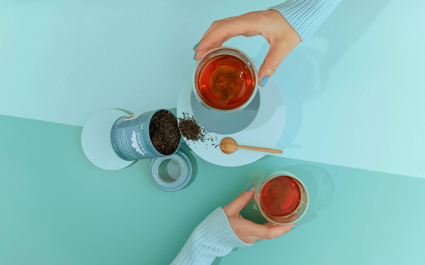Two hands holding cups of tea with a light blue background