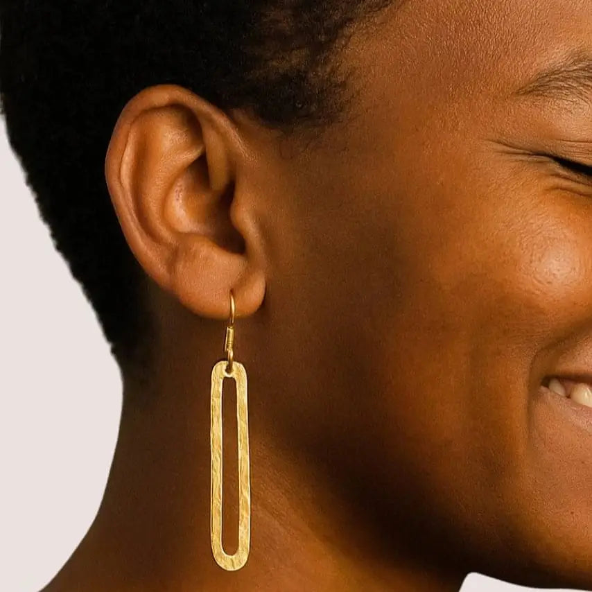 Close-up of a person wearing gold earrings with a neutral background