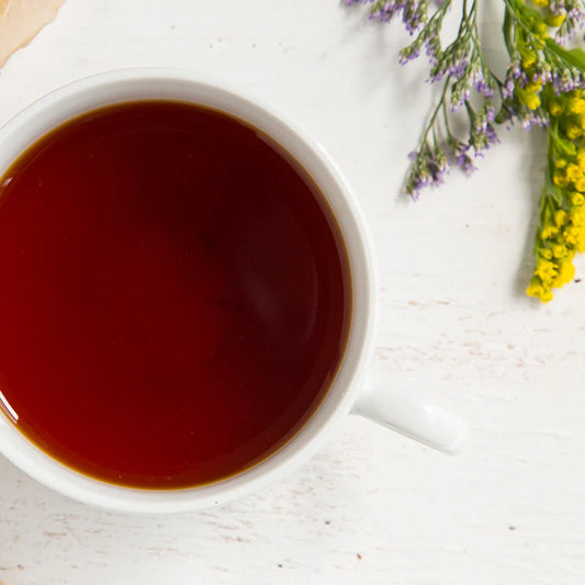 White mug filled with tea on a light wooden surface with flowers.