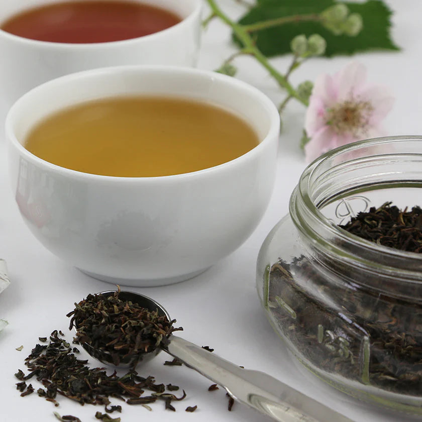 White tea cups with tea leaves and a jar of loose leaf tea on a white surface
