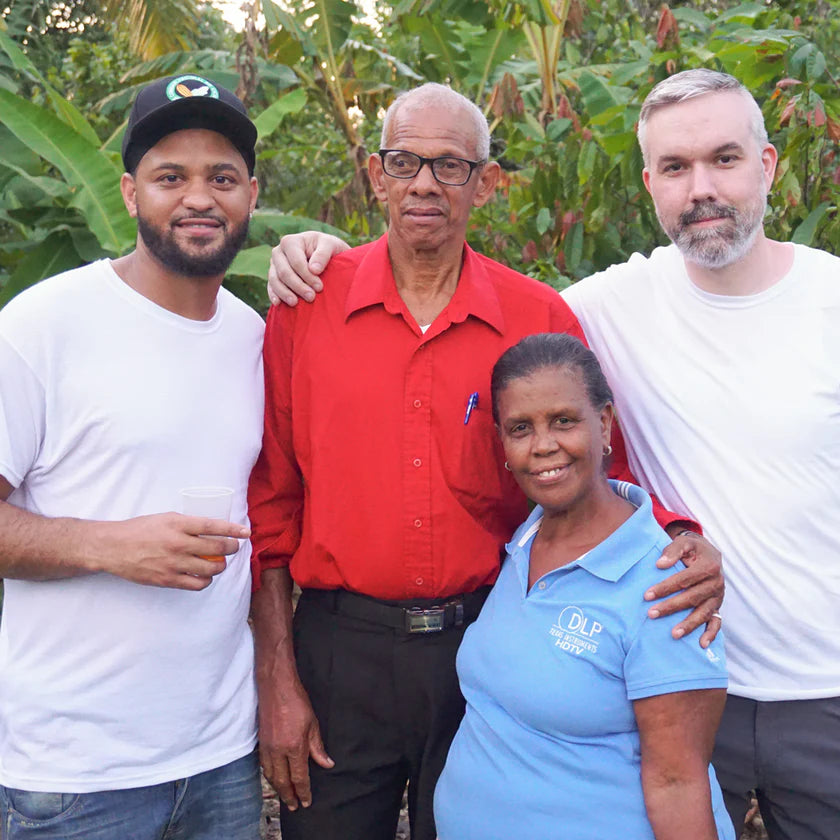 Four people posing together outdoors with cacao trees in the background