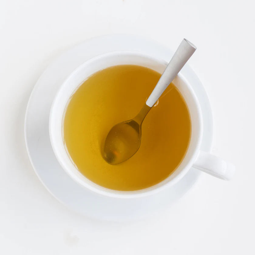 White cup with peppermint tea and a spoon on a white background