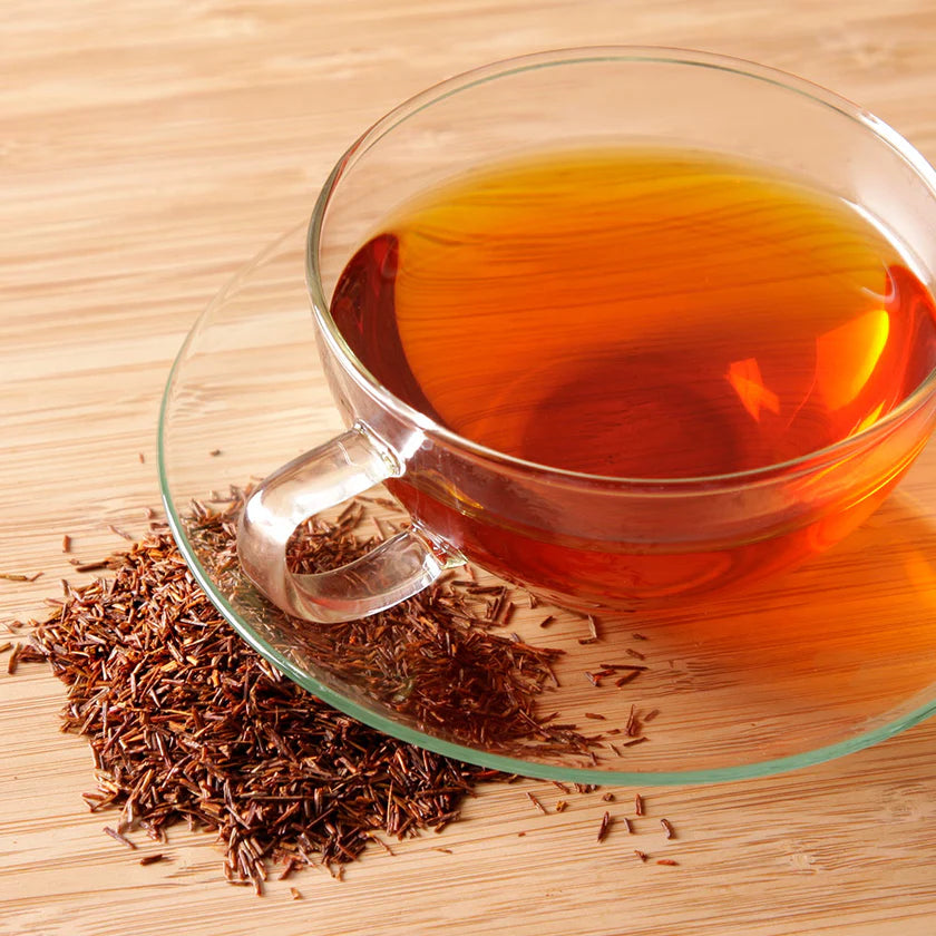 Clear glass mug filled with red tea and tea leaves on a wooden surface